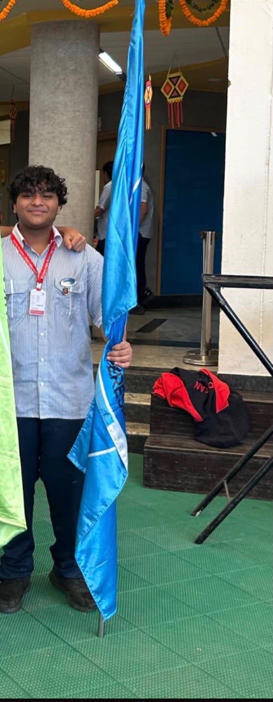 Smyan Bansal in school uniform holding a light-blue flag, smiling
