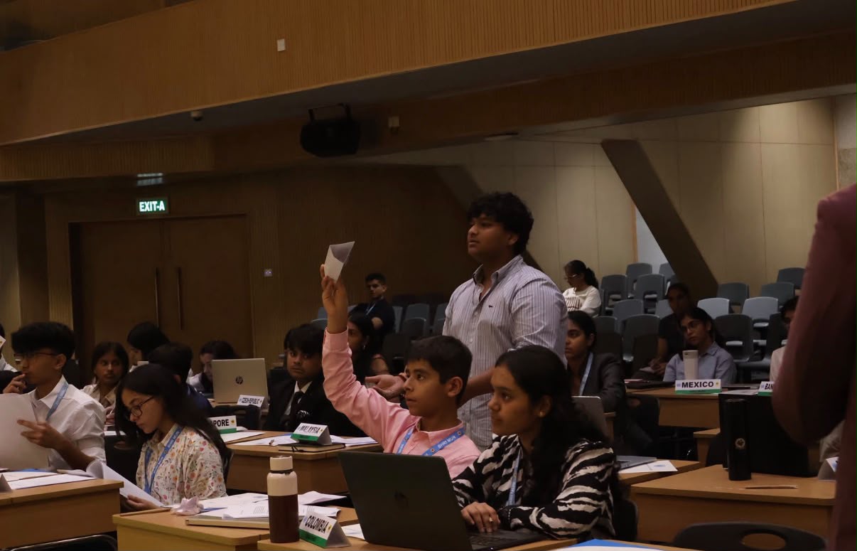 Smyan Bansal standing during a Model UN committee session among delegates and country placards